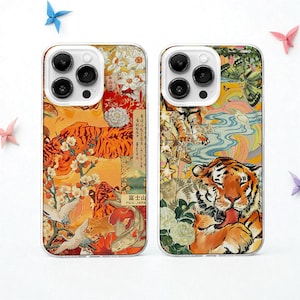 May include: Two phone cases with a vibrant, artistic design featuring tigers, flowers, and Japanese-inspired elements. The cases have a clear border and a collage-like aesthetic with orange, white, and blue hues. The design includes text and illustrations.
