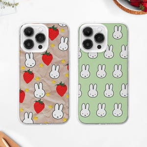 May include: Two phone cases with clear borders. One case features a pattern of red strawberries, white bunny faces, and yellow stars on a brown background. The other case has a pattern of white bunny faces on a light green background.