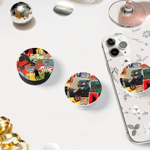 May include: Two phone grips with colorful, abstract designs featuring black cats. One grip has a black cat with a red ribbon and the other has a blue cat with a red and white striped ribbon.