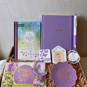 May include: A gift box containing a 365 Daily Devotions book, a purple Notes journal with a matching pen, a prayer card gift set, a purple beaded bracelet, a scalloped purple trinket dish with gold text, and three small decorative cards.
