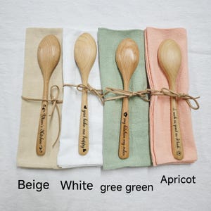 Puede incluir: Cuatro cucharas de madera con diferentes lemas grabados. Las cucharas están envueltas en servilletas beige, blanca, verde y albaricoque. Los lemas son "Cocina de mamá", "Me haces feliz", "Mi cocina, mis reglas" y "Cocino tan bien como me veo".