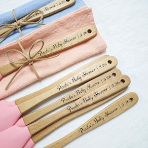 May include: Five wooden spatulas with pink silicone heads. Each spatula is engraved with the text "Paula's Baby Shower | 3.26".