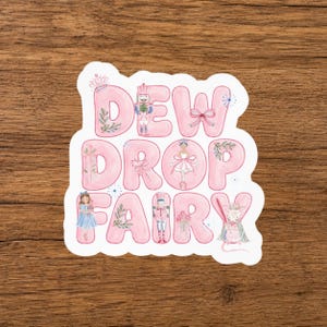 May include: A die-cut sticker featuring the text DEW DROP FAIRY in large, bubble-style pink letters. The design incorporates watercolor illustrations of a nutcracker, a ballerina, a mouse, and floral accents integrated into the lettering.