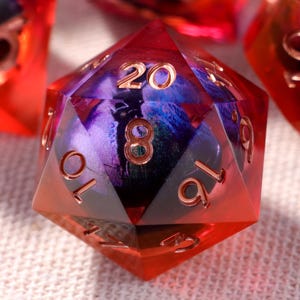 Könnte beinhalten: Ein Satz Würfel in Rot- und Lilatönen mit goldenen Zahlen. Die Würfel bestehen aus einem durchscheinenden Material. Geeignet für Rollenspiele und Brettspiele.