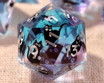 May include: A set of polyhedral dice made from translucent blue and purple resin. Each die features embedded black cat silhouettes and silver-colored numbers. The dice have sharp edges and a glossy finish, with various shapes including twenty-sided, twelve-sided, and eight-sided forms visible in the collection.