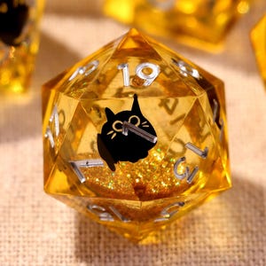 Puede incluir: Conjunto de dados dorados y facetados con una silueta de gato negro en su interior. Los dados tienen números plateados y detalles de purpurina. Dados transparentes para juegos de mesa.