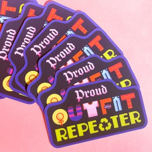 May include: A stack of stickers with a black background and a purple border. The stickers have the words "Proud Outfit Repeater" in various colors. The design includes a hat, shirt, pants, and a recycling symbol. The background is pink.