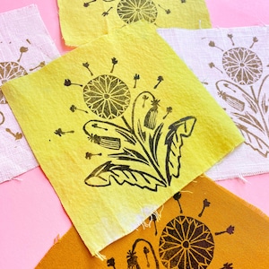 May include: Four fabric squares with a black dandelion print. The squares are yellow, white, and orange.