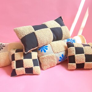 May include: Four decorative pillows with a checkered pattern in black and cream. The pillows are made of a fluffy, textured fabric and have embroidered floral designs in blue and red.