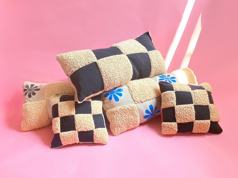 May include: Four decorative pillows with a checkered pattern in black and cream. The pillows are made of a fluffy, textured fabric and have embroidered floral designs in blue and red.