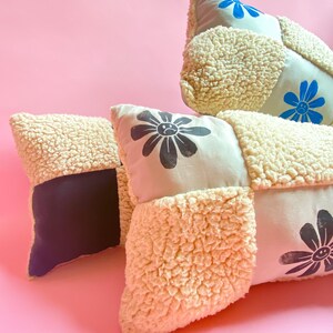 May include: Three decorative pillows with a patchwork design. The pillows are made of a soft, fluffy material and feature black and blue flower designs.