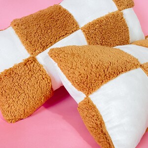 May include: Two brown and white checkered throw pillows with a fuzzy texture. The pillows are made of a soft, plush fabric.