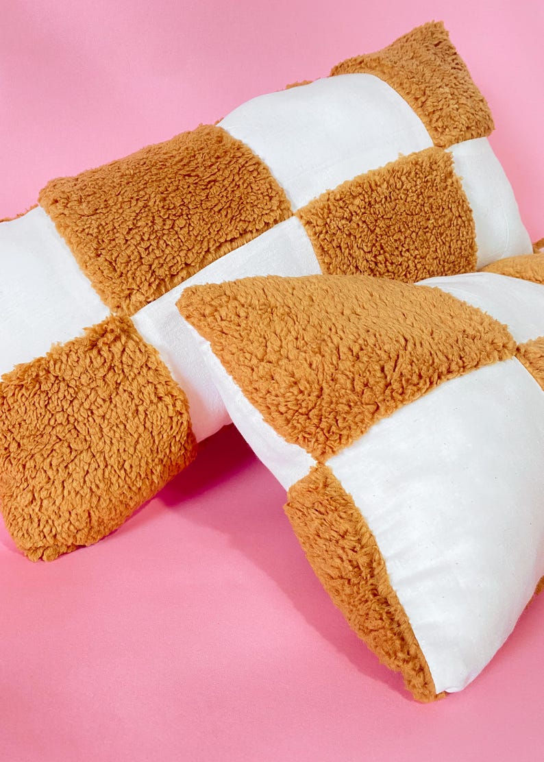 May include: Two brown and white checkered throw pillows with a fuzzy texture. The pillows are made of a soft, plush fabric.