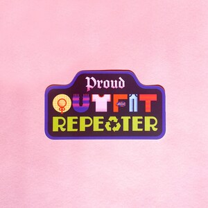 May include: A rectangular sticker with a black border and the words "Proud Outfit Repeater" in white and green. The word "Outfit" is represented by colorful icons of clothing items. The background is a solid light pink.