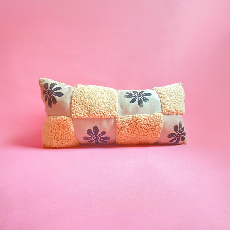 May include: A long, rectangular pillow with a patchwork design. The pillow is made of a soft, cream-colored fabric with black flower designs.
