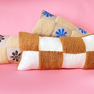 May include: Three decorative pillows with a patchwork design. The pillows are made of a soft, fluffy material and feature different colored squares and embroidered flowers.