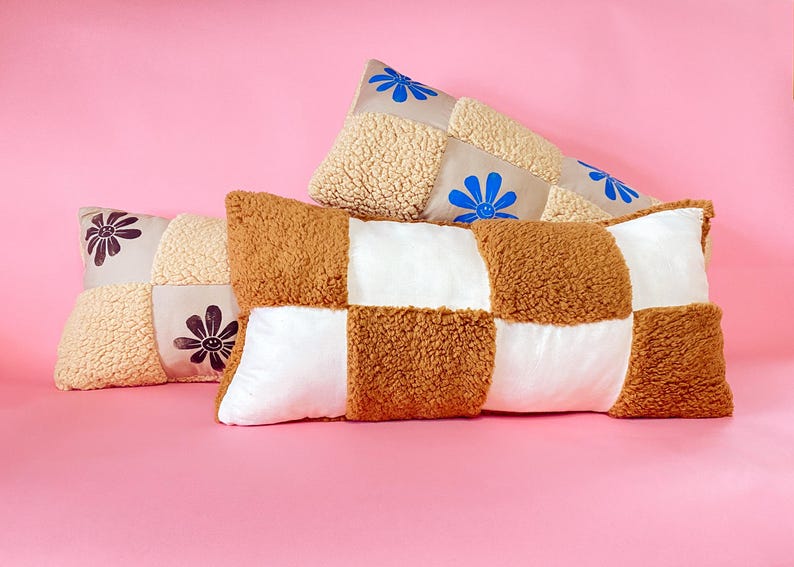May include: Three decorative pillows with a patchwork design. The pillows are made of a soft, fluffy material and feature different colored squares and embroidered flowers.