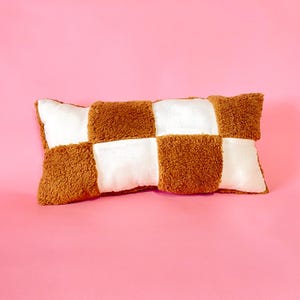 May include: A brown and white checkered pillow with a soft, fuzzy texture. The pillow is rectangular and has a slightly rounded shape.