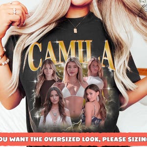 May include: Black t-shirt with the name "CAMILA" in gold lettering. The shirt features a graphic of several women. The text at the bottom reads "IF YOU WANT THE OVERSIZED LOOK, PLEASE SIZING UP".