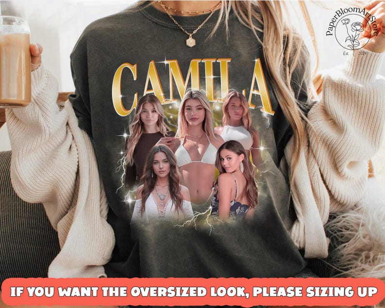 May include: Dark green sweatshirt featuring the name "CAMILA" in gold lettering with a vintage design. The sweatshirt has a graphic of five women and lightning bolts. The text at the bottom reads "IF YOU WANT THE OVERSIZED LOOK, PLEASE SIZING UP."