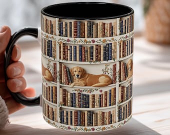 May include: A black-handled coffee mug featuring a wrap-around design of a bookshelf filled with books. A golden retriever is resting on one of the shelves. The mug has a black interior and is held by a person wearing a beige sweater.
