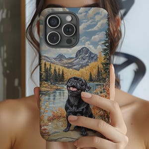 May include: A phone case featuring a painting of a black pug dog sitting by a lake with mountains in the background. The artwork has a landscape theme with autumn colors.