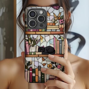 May include: A phone case with a stained-glass effect depicting a bookshelf with a sleeping black cat. The case features colourful books, flowers, and butterflies. The case is held in front of a person.