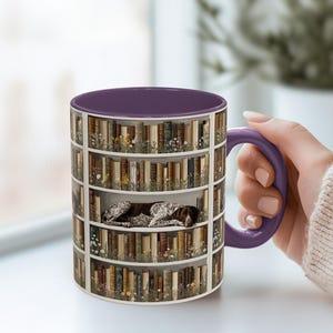 May include: A ceramic mug with a purple interior and handle. The exterior features a bookshelf design with old books and flowers. A brown and white dog is nestled in one of the shelves. The mug is held by a person.