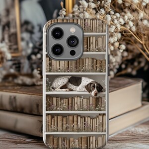 May include: A phone case with a bookshelf design, featuring a German Shorthaired Pointer dog. The case shows a white bookshelf filled with old books and small flowers. The dog has brown and white spots.