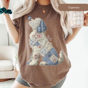May include: An espresso brown t-shirt featuring a large graphic of a dog composed of blue and white floral and plaid patchwork patterns. A small blue butterfly rests on the dog's nose, and the name Molly is printed in white script near the dog's back.