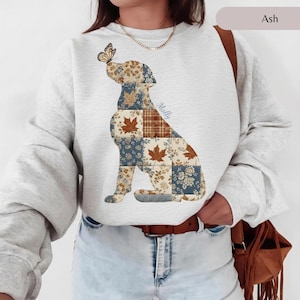 May include: An ash gray crewneck sweatshirt featuring a large graphic of a sitting dog composed of various patchwork squares with floral, plaid, and maple leaf patterns. A small butterfly rests on the dog's nose, and the name Molly is printed.