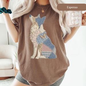 Könnte beinhalten: Espressofarbenes T-Shirt mit einem Wolf-Patchwork-Design. Der Wolf besteht aus verschiedenen Stoffmustern, darunter Blumenmuster, Karomuster und Denim, mit einem hölzernen Schmetterlingsakzent. Das Shirt hat eine bequeme, übergroße Passform.