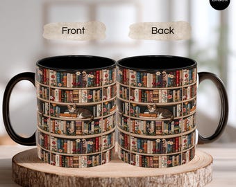 May include: Black coffee mug featuring a bookshelf design with a cat resting on a shelf. The mug has a black interior and handle. The bookshelf is filled with colorful books and flowers. The mug is sitting on a wooden slice.