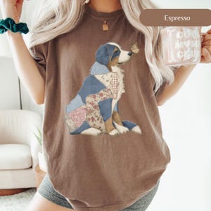 May include: Espresso-colored t-shirt featuring a patchwork dog design with blue, pink, and floral patterns. The dog has a butterfly on its nose. The shirt is a comfortable fit.
