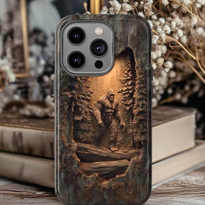 May include: A phone case with a detailed relief carving of a Bigfoot in a forest scene. The case has a textured, wood-like appearance with a brown and grey colour scheme. The design includes trees, a log, and a warm, glowing background.
