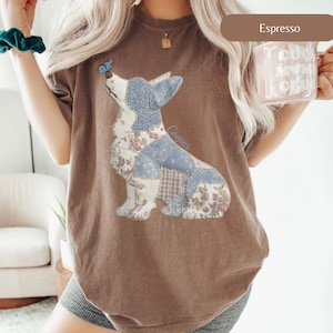 Puede incluir: Camiseta color espresso con un diseño de corgi en patchwork con patrones azules y florales, una mariposa y el nombre "Cooper". La camiseta tiene un corte holgado. Se ve una taza con el texto "Cool Mom Club".