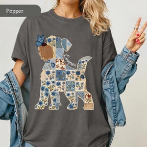 May include: A charcoal gray t-shirt featuring a graphic of a dog silhouette filled with a blue and white floral patchwork pattern. The dog has a brown tuft of hair on its head, a blue butterfly perched on its ear, and the name Cooper in script.