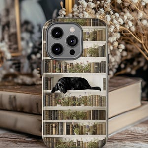 Könnte beinhalten: Eine Handyhülle mit einem Bücherregal-Design und einem schwarzen Hund, der auf einem Regal liegt. Die Hülle hat eine glänzende Oberfläche und einen Kameraausschnitt. Die Bücher sind in verschiedenen Größen und Farben.