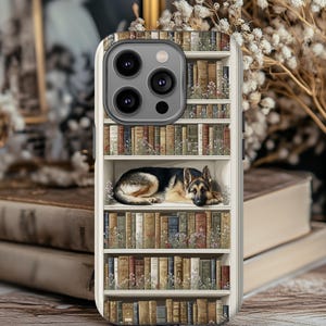 Puede incluir: Funda de teléfono con diseño de estantería y un perro pastor alemán. La funda tiene un fondo blanco con una impresión detallada de libros y flores. El perro es negro, marrón y beige, descansando en un estante.