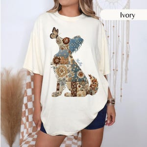 May include: An ivory short-sleeve t-shirt featuring a graphic of a sitting dog composed of various brown, blue, and cream floral and polka dot patchwork patterns. A butterfly rests on the dog's head, and the name Molly is printed in blue script.