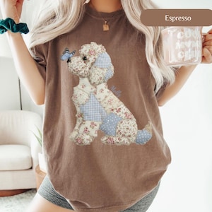 May include: Espresso-coloured t-shirt with a patchwork dog design featuring floral and gingham patterns. A blue butterfly sits on the dog's nose. The word "Molly" is written on the shirt. The shirt is a comfortable, casual style.