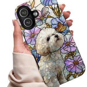 May include: A phone case featuring a white curly-haired dog surrounded by a stained glass pattern of purple, blue, and pink flowers with a small orange butterfly. The design includes dark outlines and a black camera cutout area at the top left.