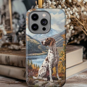 May include: A phone case with a painting of a German Shorthaired Pointer dog by a lake and mountains. The dog has a brown and white spotted coat. The case has a glossy finish and a camera cutout. The artwork evokes a scenic landscape.