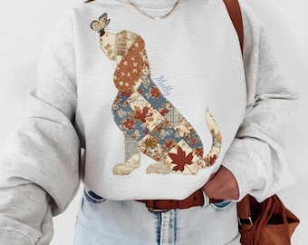 Könnte beinhalten: Ein aschgraues Sweatshirt mit Rundhalsausschnitt und einer Illustration eines Hundes im Patchwork-Stil mit Blumen- und Karomustern in Braun-, Blau- und Cremetönen. Ein Schmetterling sitzt auf der Nase des Hundes, der Name Molly steht in Blau.