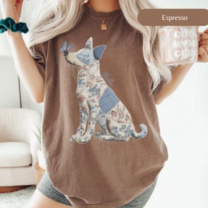 May include: Espresso-colored t-shirt featuring a patchwork dog design with a butterfly on its nose. The dog is made of floral and blue patterned fabric. The word "Molly" is written on the dog's side. The shirt is a comfortable, casual style.