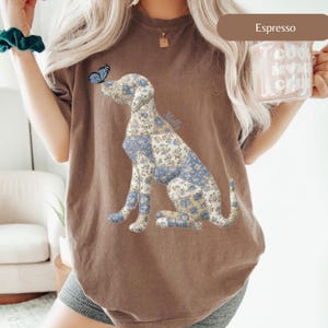 May include: Espresso-colored t-shirt featuring a seated dog graphic with a blue floral pattern. A blue butterfly rests on the dog's nose. The word "Molly" is written on the dog's side. The shirt is a comfortable, casual style.