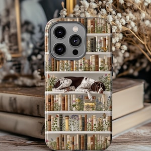 May include: A phone case featuring a detailed illustration of a bookshelf filled with books and flowers. A brown and white dog is resting on the shelves. The case has a glossy finish and a camera cutout.