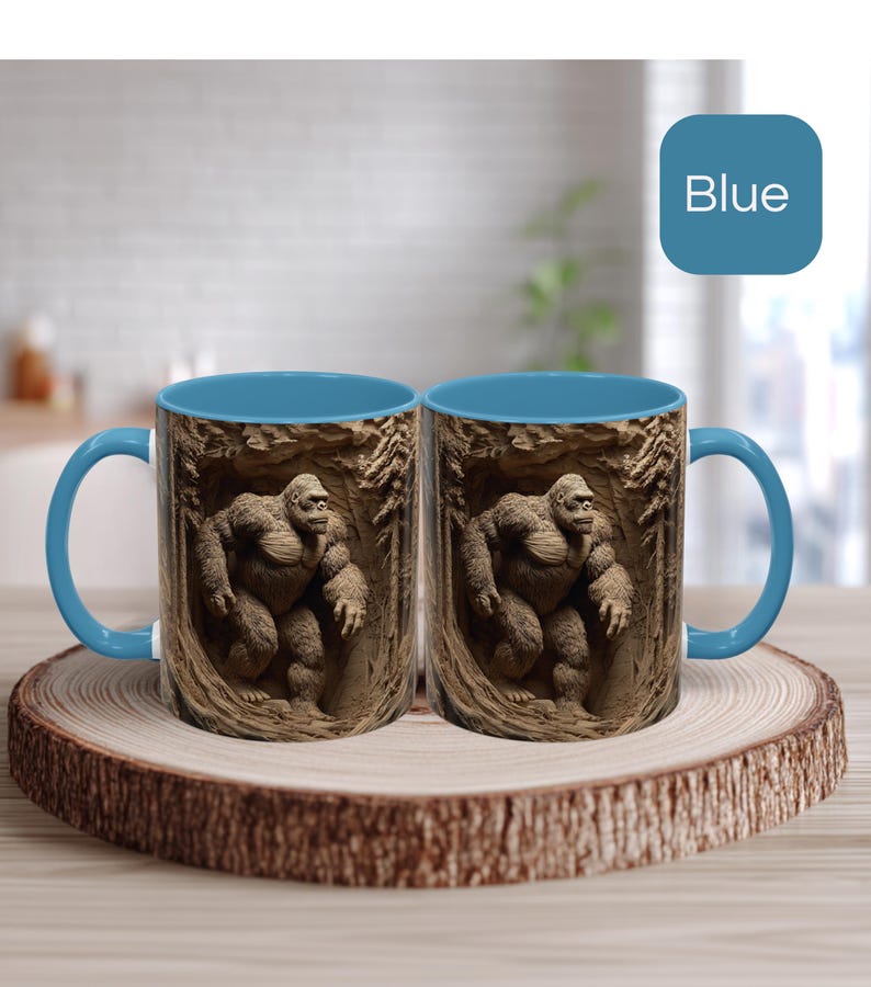 May include: Two blue-handled coffee mugs with a detailed image of a gorilla in a cave setting. The mugs have a blue interior and are displayed on a wooden coaster. The word "Blue" is in a blue square in the background.