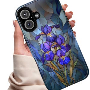 May include: A smartphone case featuring a stained glass design with vibrant purple iris flowers and green stems set against a background of blue and grey geometric glass panels. The case has a black camera module cutout with two circular lenses.