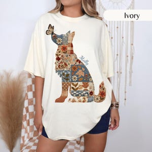 May include: An ivory short-sleeve t-shirt featuring a large graphic of a dog silhouette filled with a multi-coloured patchwork pattern of flowers, leaves, and plaid. A butterfly rests on the dog's nose, and the name Molly is printed in script.